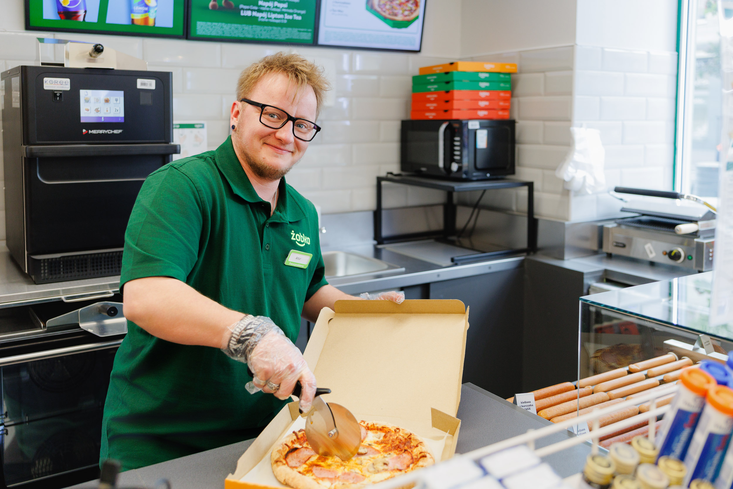 Artur slicing fresh pizza in a Żabka convenience store in Gdynia during food preparation