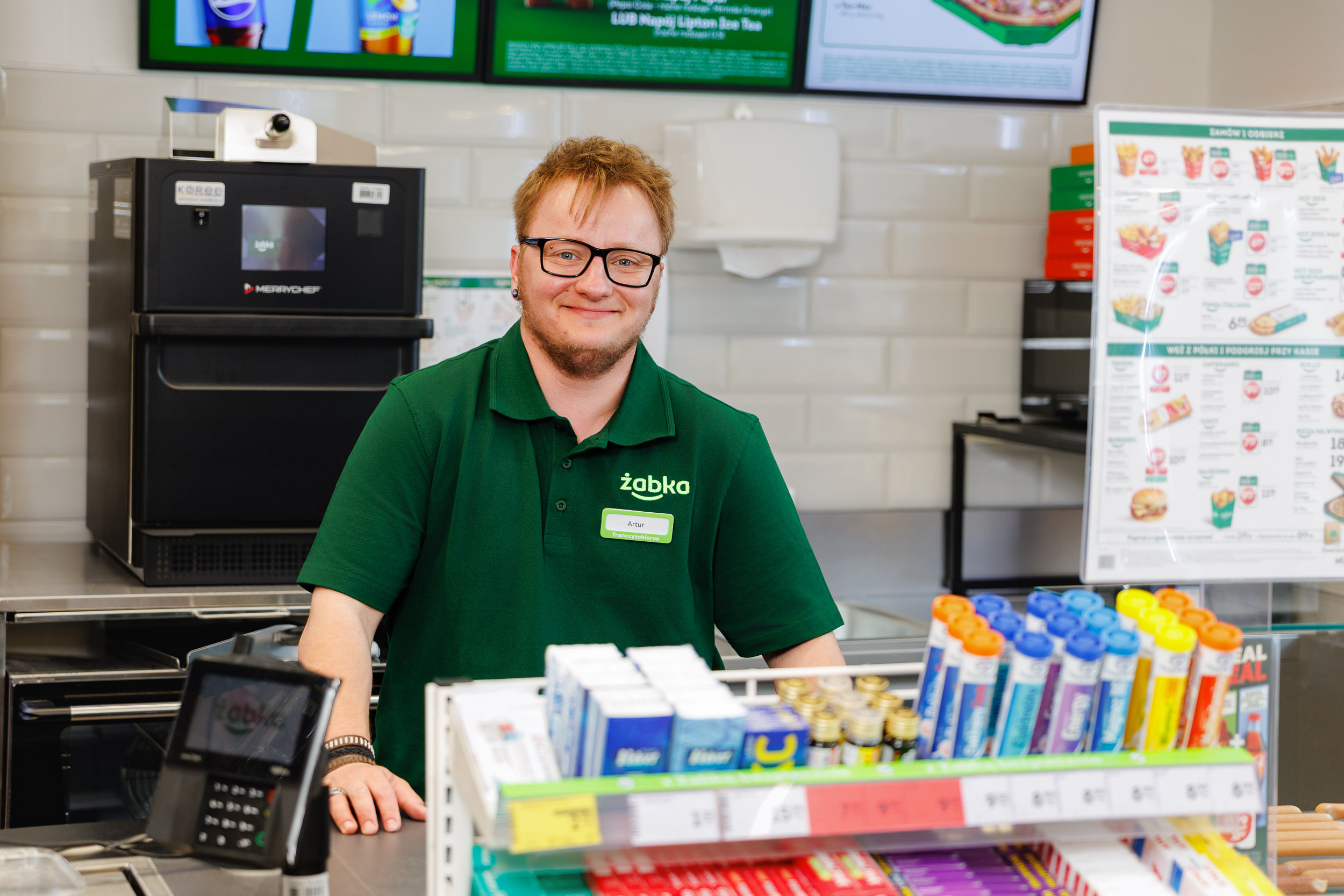 Franchise owner Artur working at the checkout in a Żabka store in Gdynia during daily operations