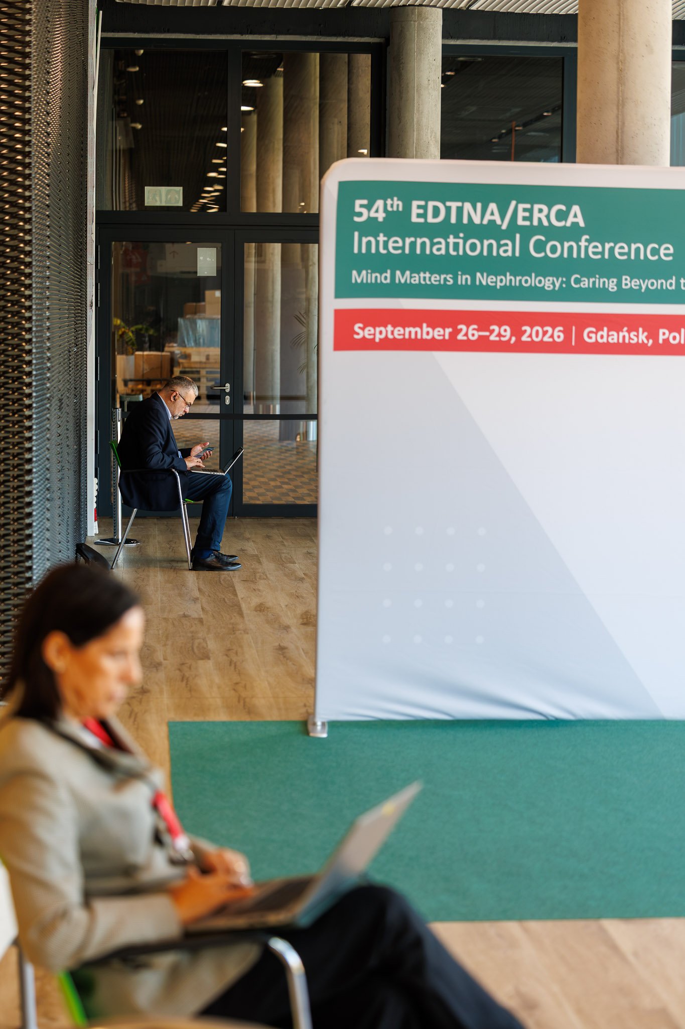 Uczestnik konferencji pracuje na laptopie obok ścianki konferencyjnej w foyer AmberExpo w Gdańsku