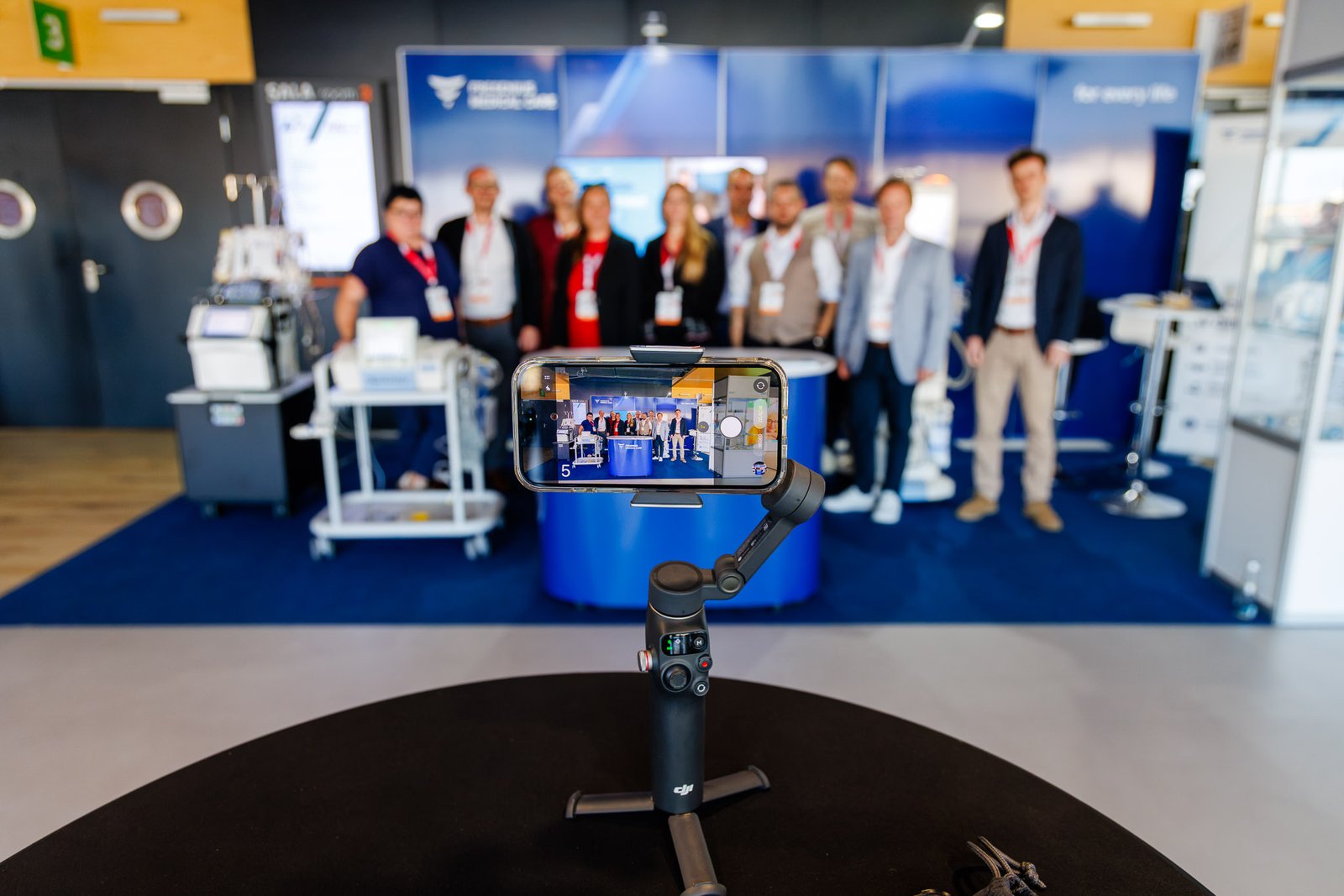 Conference attendees taking a group selfie with a phone on a DJI gimbal in the exhibition area